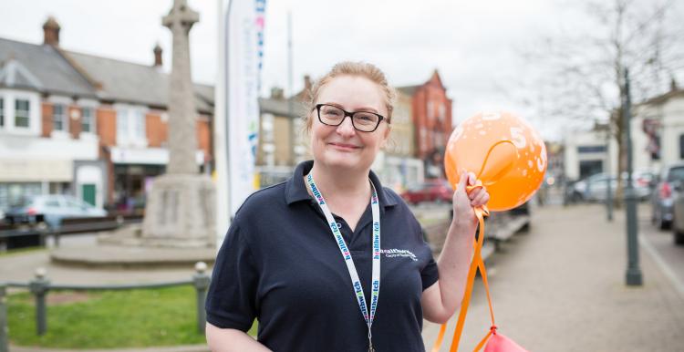 Female volunteer standing in front of a Healthwatch flag holding two balloons